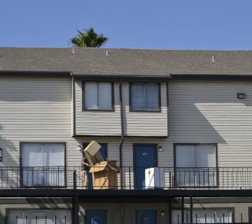 A person sitting on a balcony of an apartment building under a clear sky.